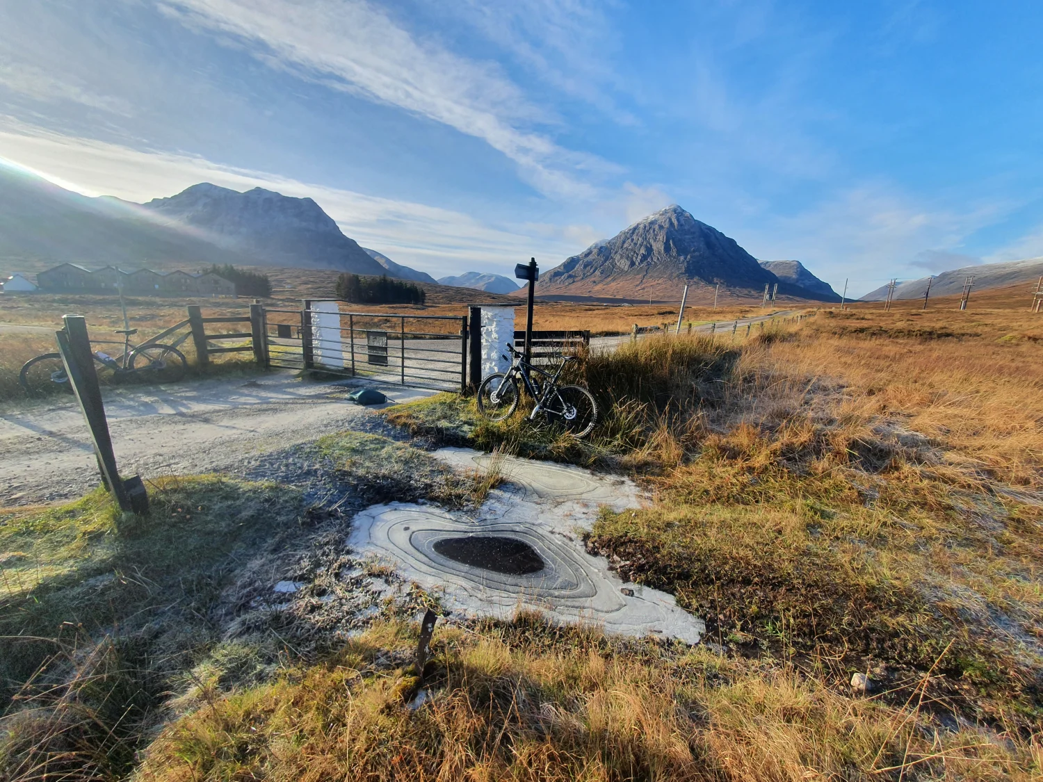 The gated start of the Black Corries track on a frosty morning, mountain bikes propped against the fence with Buachaille Etive Mòr rising beyond
