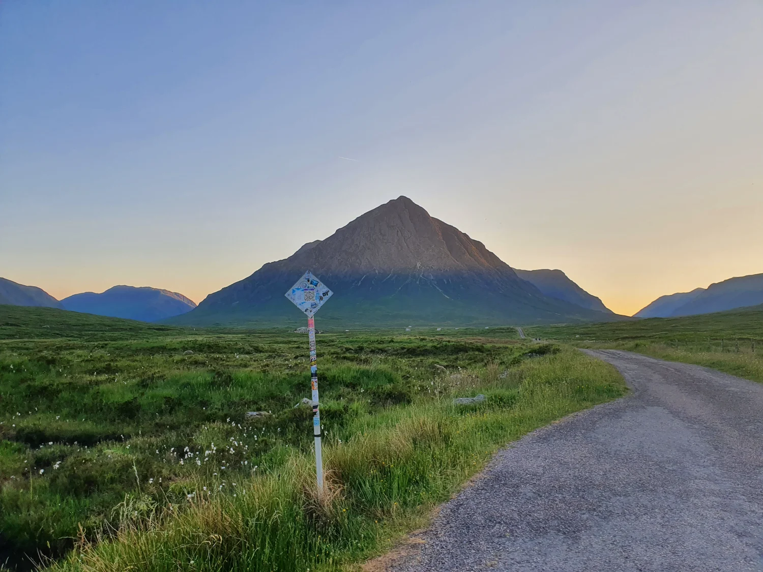 A waymarker post on the old military road with Buachaille Etive Mòr catching the last light of the day beyond