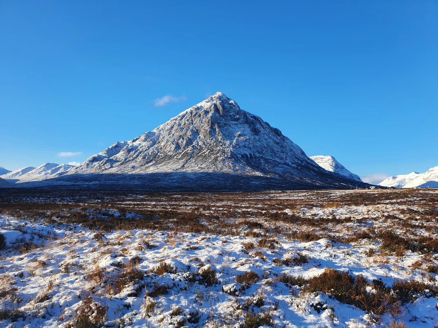 A snow-capped Buachaille Etive Mòr rising above a frozen, snow-dusted moor under clear winter skies