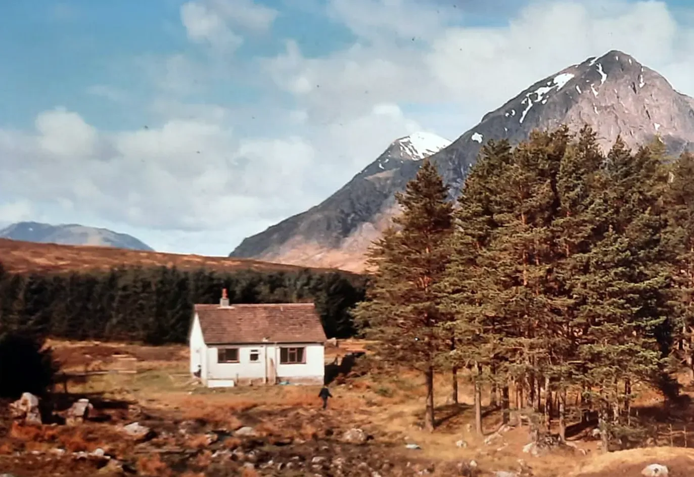 The cottage in the early 1990s: a white bungalow with a red tiled roof standing among pines below the mountain